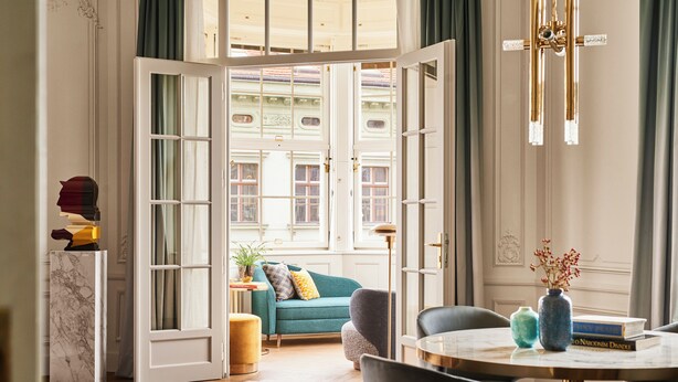 A room with a large open door leading to a balcony, a sofa, a coffee table, and a vase with flowers. - ANDAZ PRAGUE, BY HYATT (Prague)