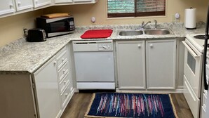 Une cuisine de taille réduite avec des meubles blancs, un four à micro-ondes, un grille-pain, un évier et une fenêtre équipée de stores.
