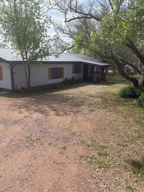 A single-story building with a metal roof, a visible number '1055' on the side, and a gravel driveway. - Make Memories in this Comfy Two Bedroom Two Bath Home (Pine)