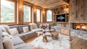 Un salon chaleureux avec une cheminée en pierre, des murs en bois et une grande fenêtre donnant sur un paysage verdoyant.
