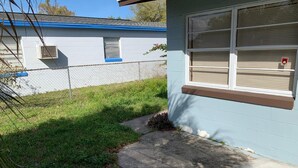 A residential building with a blue exterior, a concrete pathway leading to the entrance, and a fenced backyard.