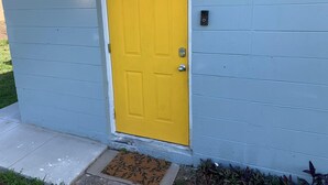 A yellow door with a doormat and a wall-mounted light fixture.