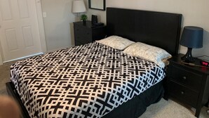 A bedroom with a bed, a nightstand, a lamp, a clock, and a door.