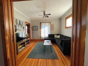 Una sala de estar con televisor, un sofá negro, una mesa de centro y un ventilador de techo.
