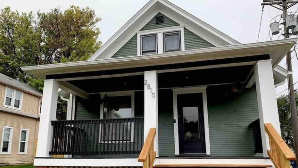A two-story house with a front porch, a visible number '2810' on the door, and a small dog inside.