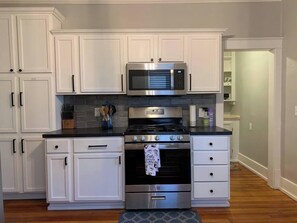 Una cocina con armarios blancos, un microondas de acero inoxidable y un horno.