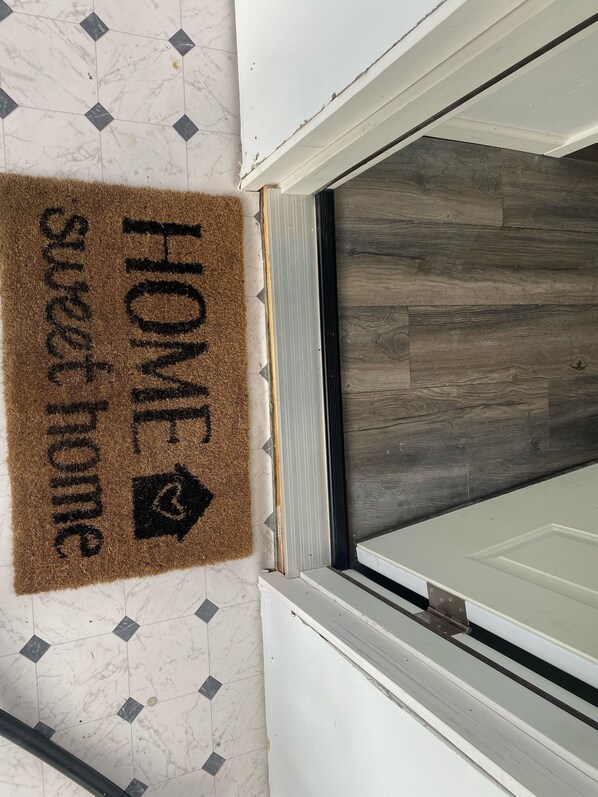 A doormat with "HOME sweet home" text and a house icon, a white door with a window, and a wooden floor.
