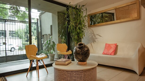 A modern living room with a round coffee table, two yellow chairs, a white sofa with a pink pillow, and a large potted plant. - Capital O Hotel Terraza 158 Mexico City (Mexico City)