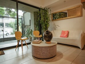 A modern living room with a round coffee table, two yellow chairs, a white sofa with a pink pillow, and a large potted plant.