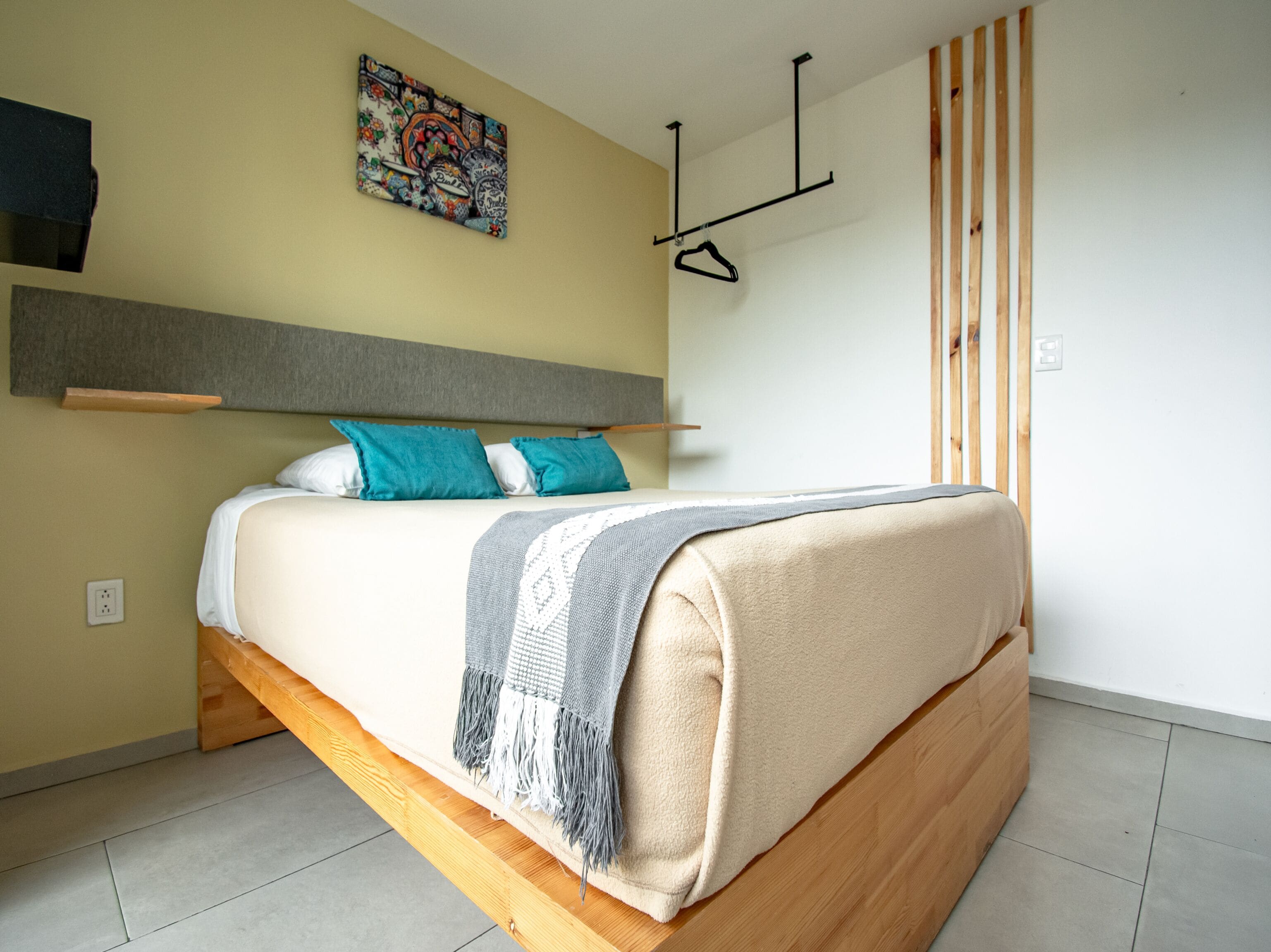 Une chambre à coucher moderne avec un cadre de lit en bois, une tête de lit grise et un tableau abstrait coloré accroché au mur.