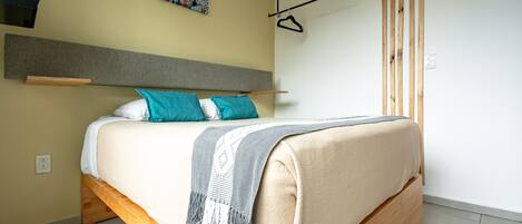 Une chambre à coucher moderne avec un cadre de lit en bois, une tête de lit grise et un tableau abstrait coloré accroché au mur.