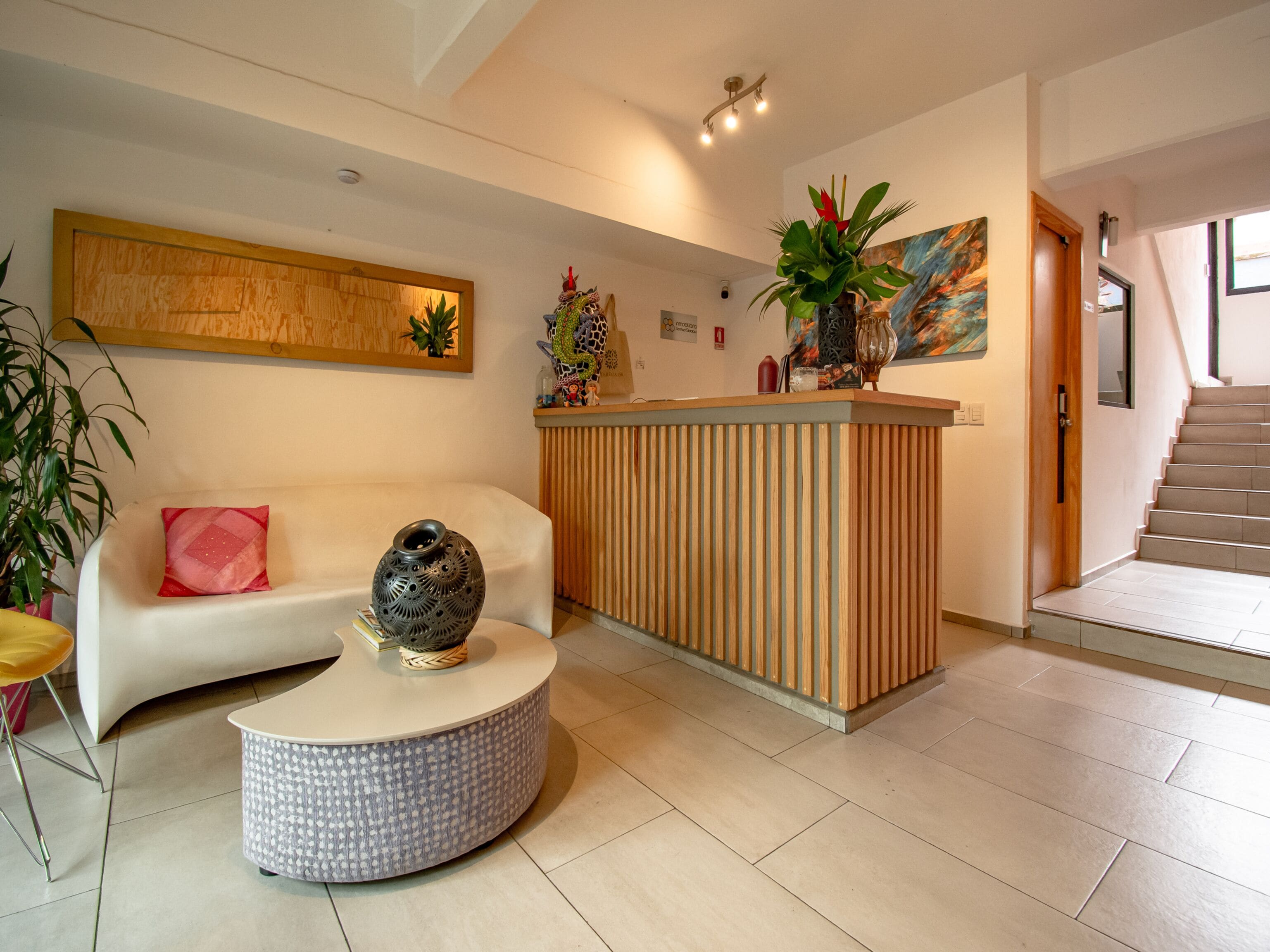 A modern reception area with a white sofa, a round coffee table, a wooden reception desk, and a staircase leading upstairs.