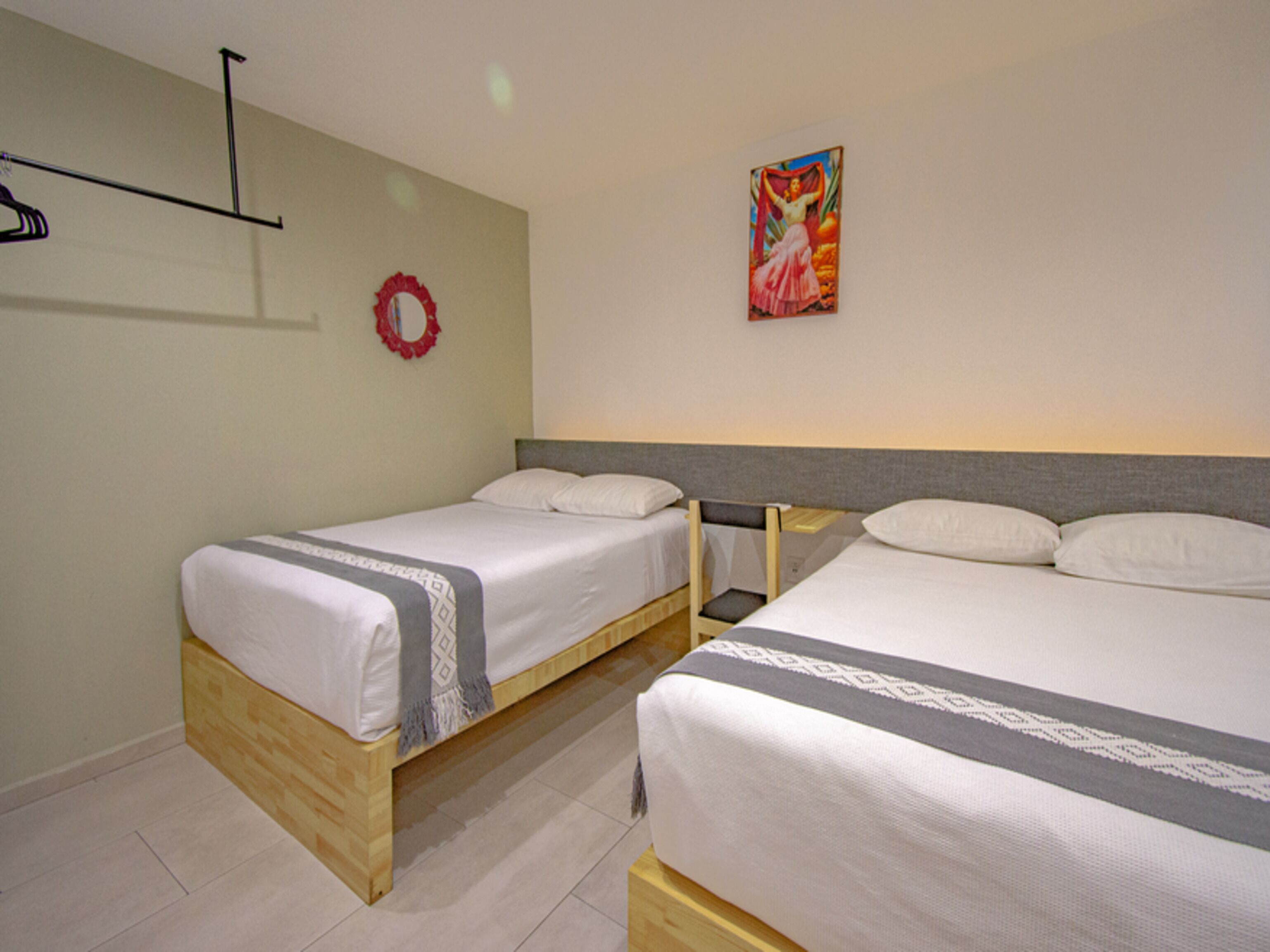 Habitación de hotel con dos camas individuales, cabecero de madera, una mesita y una estantería en la pared.