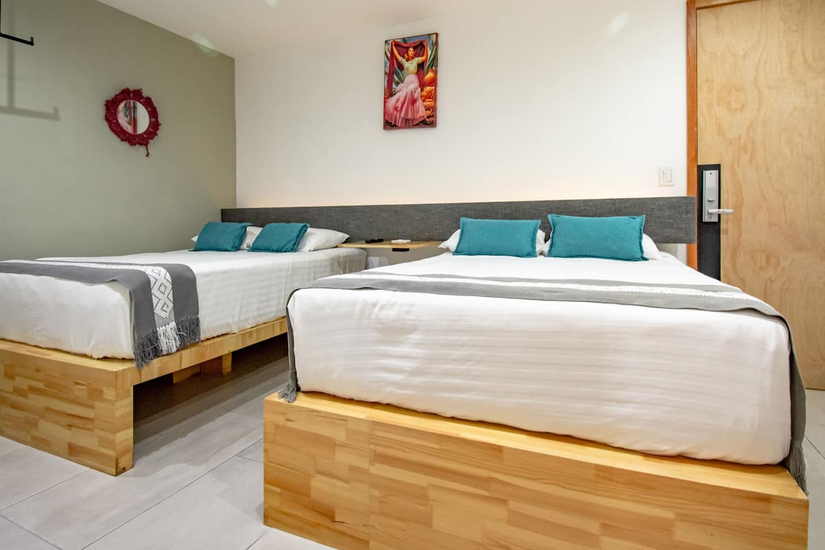 A hotel room with two wooden beds, white bedding, teal pillows, a red wreath on the wall, and a painting above the beds.