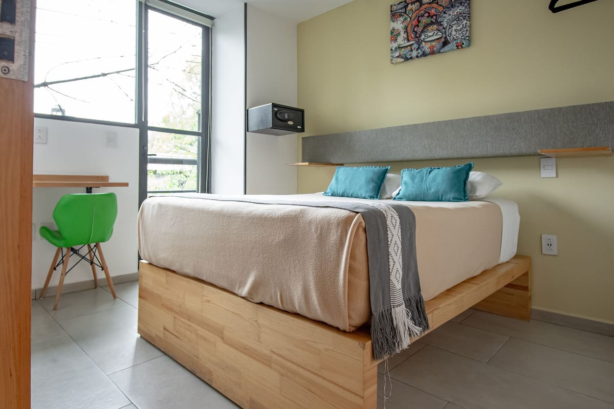 A modern bedroom with a wooden bed, a green chair, a desk, and a large window.