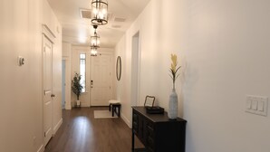 A hallway with wooden flooring, white walls, a black console table with a vase, and a door at the end. - NEW Flagstaff single-story home with a beautiful backyard and Hot Tub! (Flagstaff)