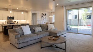 A modern living room with a grey sectional sofa, a round coffee table, and a kitchen in the background. - NEW Flagstaff single-story home with a beautiful backyard and Hot Tub! (Flagstaff)