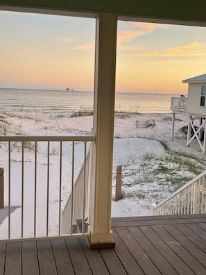 Une terrasse en bois dotée d’une rambarde, qui offre une vue sur une plage de sable où la végétation est clairsemée.