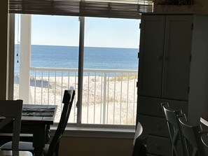 Ein Zimmer mit großem Fenster und Blick auf einen Strand. Es gibt einen Tisch mit Stühlen und einen Schrank.