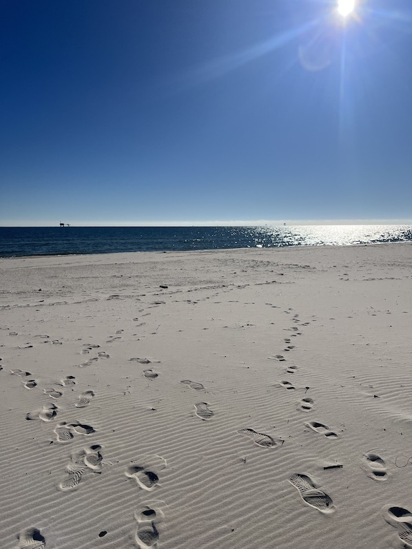 Une plage avec des empreintes de pas dans le sable et un ciel dégagé.