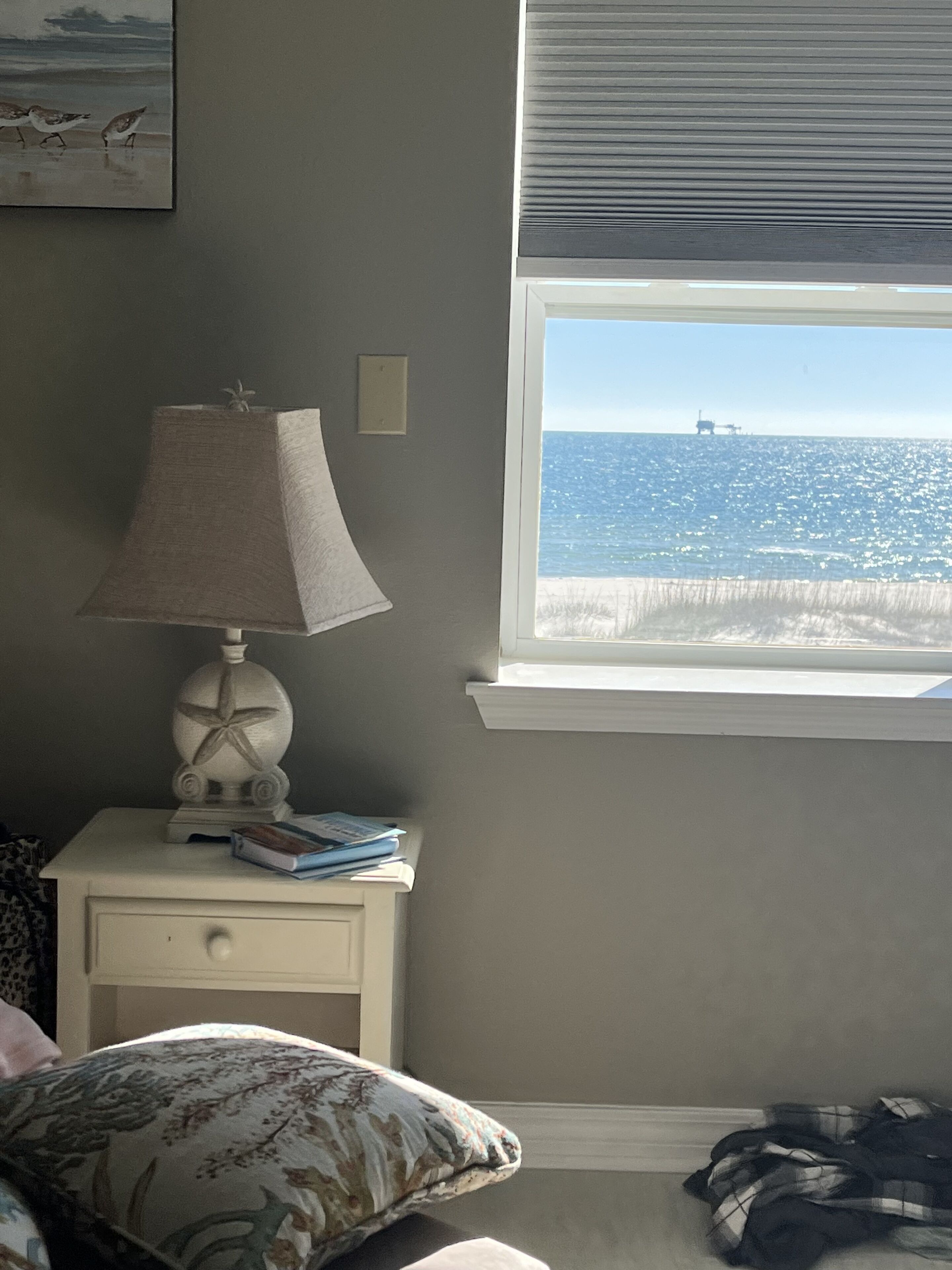A bedroom with a window overlooking the beach, a bedside lamp, and a nightstand with books.