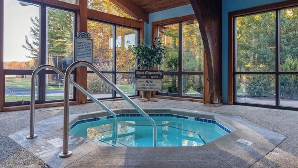 An indoor pool area with a wooden ceiling, large windows, and a sign indicating spa capacity. - Cozy Canadian Lakes Cottage (Canadian Lake)