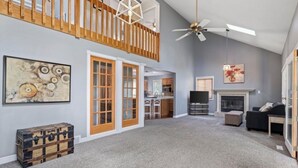 A spacious living area with a high ceiling, a fireplace, a ceiling fan, and a staircase leading to an upper level. - Cozy Canadian Lakes Cottage (Canadian Lake)