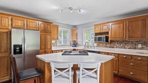 A kitchen with wooden cabinets, a stainless steel refrigerator, a microwave, a sink, and a white island with chairs. - Cozy Canadian Lakes Cottage (Canadian Lake)