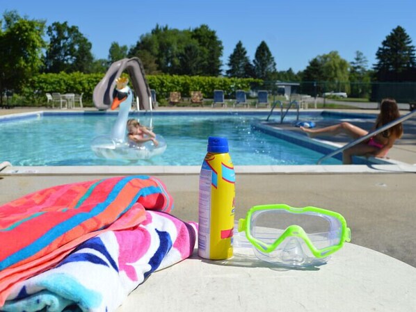 A poolside area with a towel, sunscreen, and swim goggles on a table.