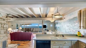 A spacious living area with a stone fireplace, a red sofa, and a kitchen with a dishwasher. - Breathtaking Beach Front House - Steps to the Sand (Aptos)
