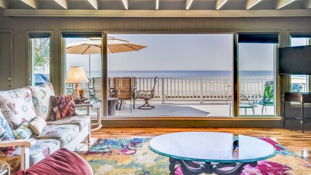 A spacious living room with a large glass door leading to a balcony with a view of the sea. - Breathtaking Beach Front House - Steps to the Sand (Aptos)
