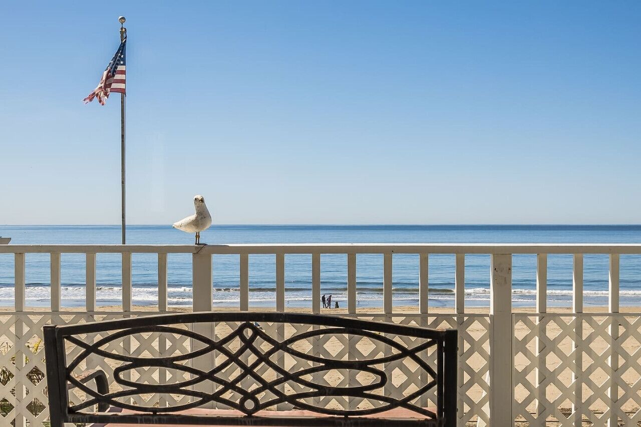 Vista de la playa con una valla blanca, una bandera y una silla.