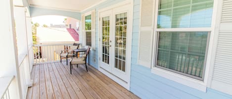 Um deck de madeira com mesa e cadeiras, persianas brancas e vista para a rua.