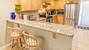 Una cocina con armarios de madera, encimera de granito, refrigerador de acero inoxidable y dos taburetes de mimbre.
