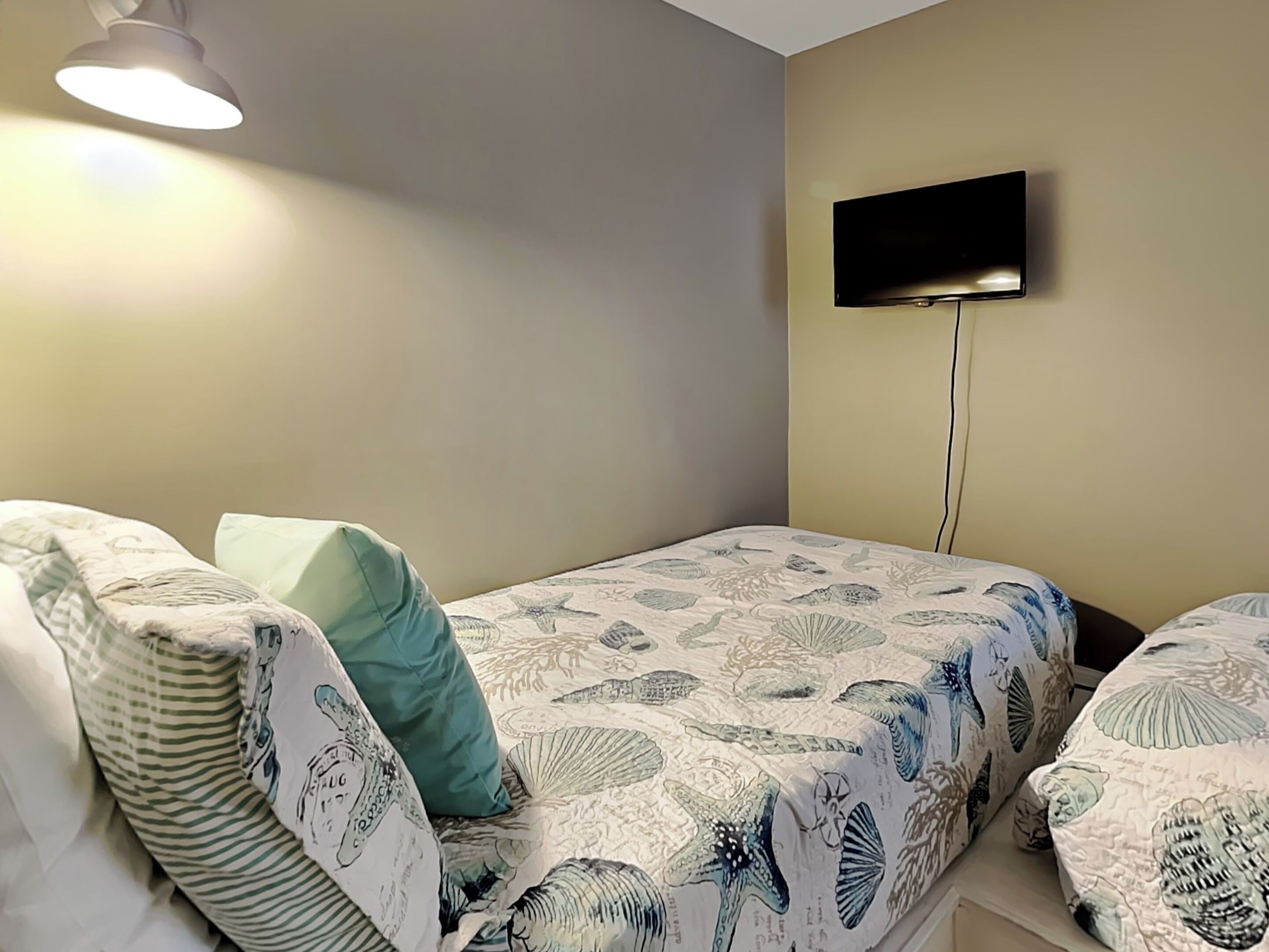 A bedroom with two beds, each with patterned bedding and pillows. A flat-screen TV is mounted on the wall above one bed.