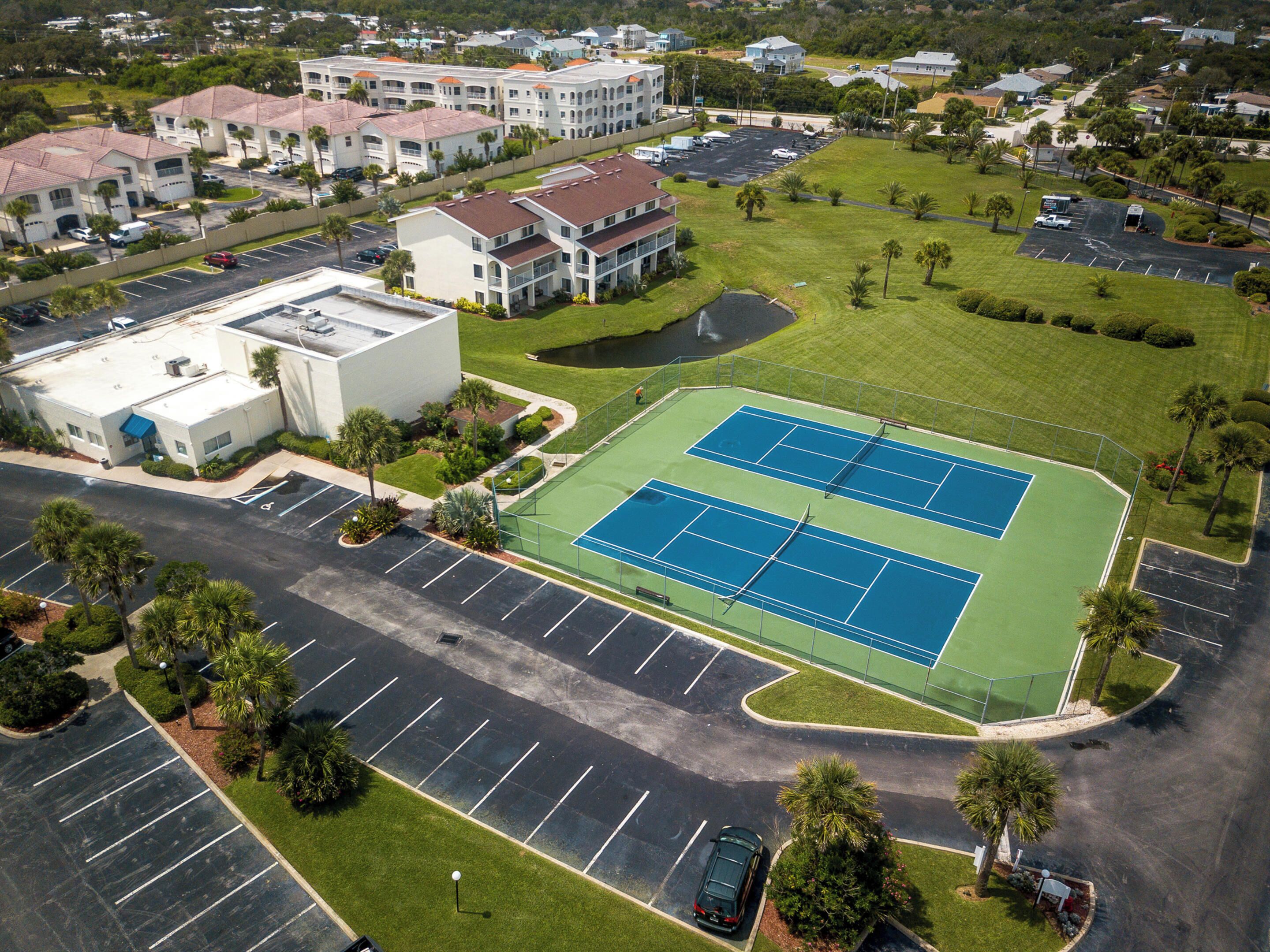 Vista aérea de una zona residencial con cancha de tenis, estacionamientos y edificios circundantes.