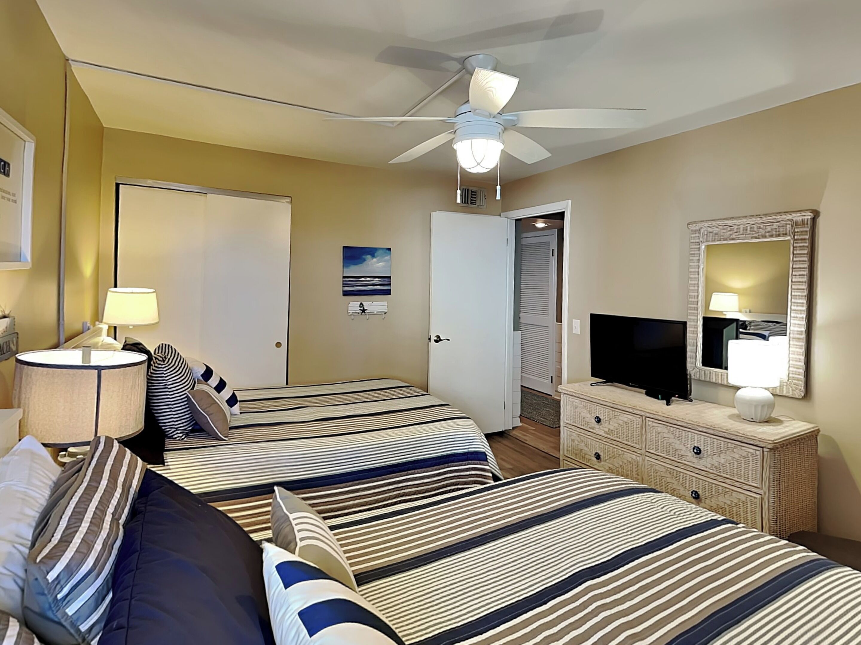 A hotel room with two beds, a ceiling fan, a television, a dresser, and a door leading to a closet.