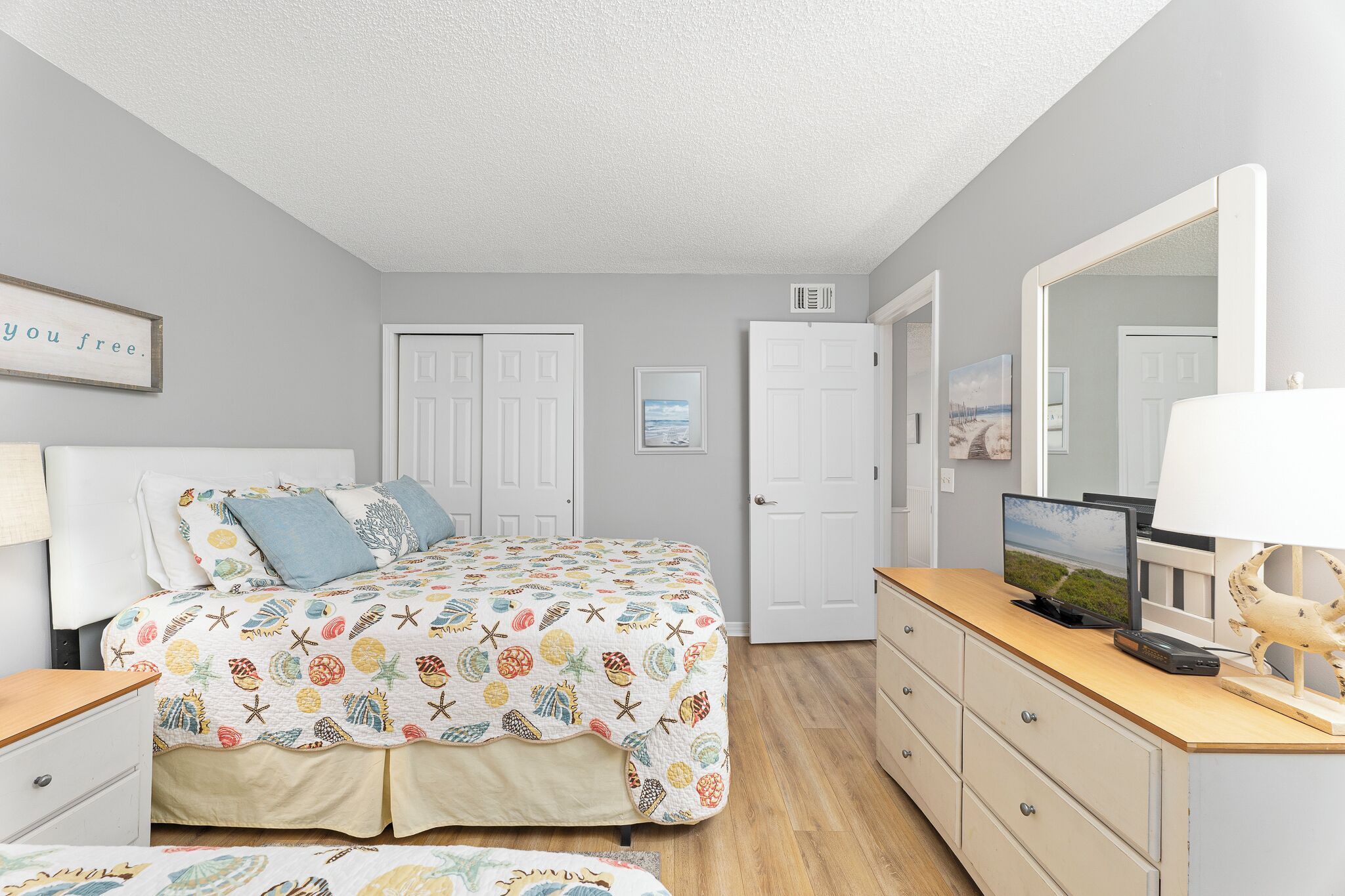 A bedroom with a bed, dresser, TV, and a mirror.