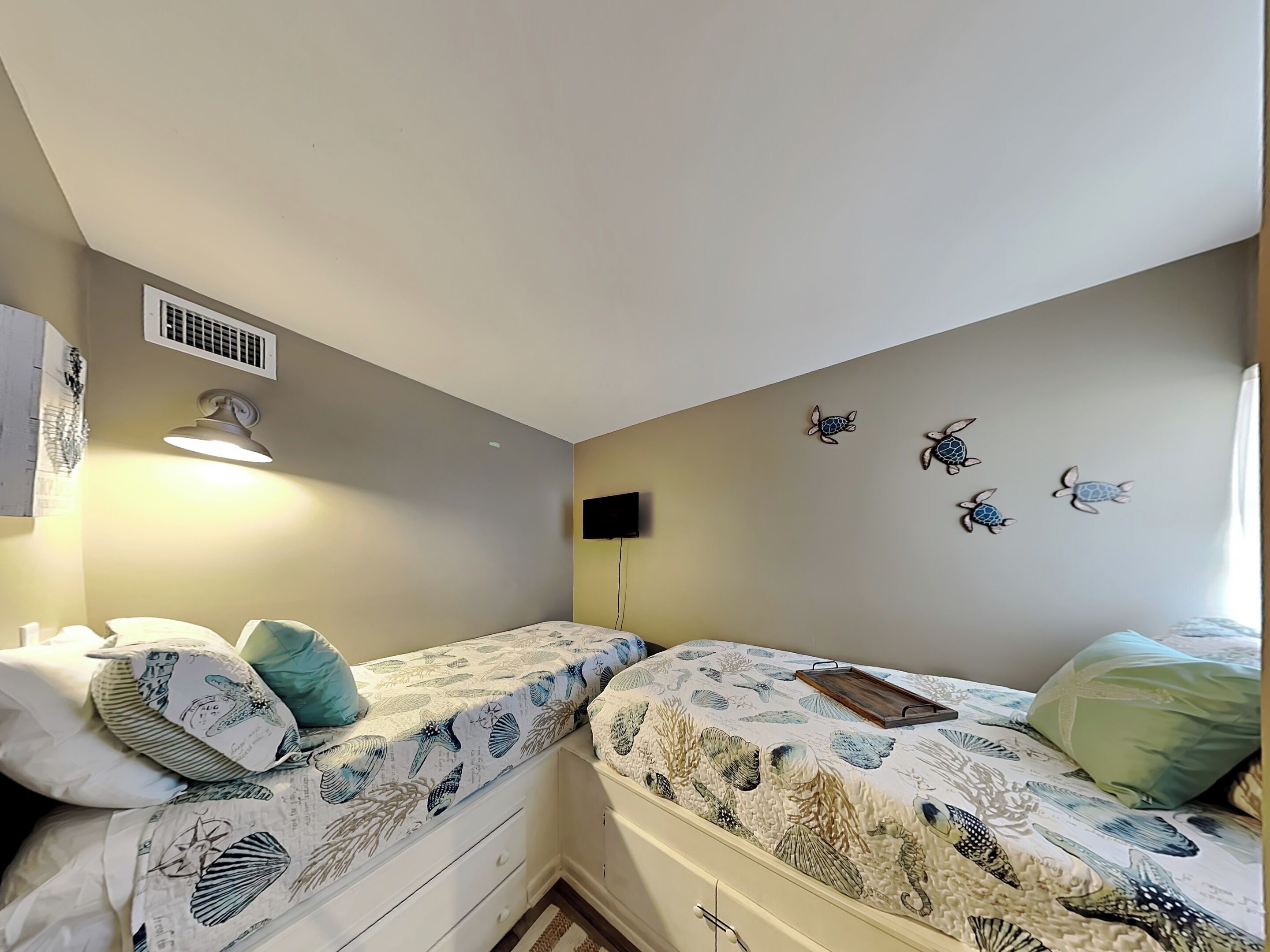 A bedroom with two beds, a wall-mounted TV, and a ceiling vent.