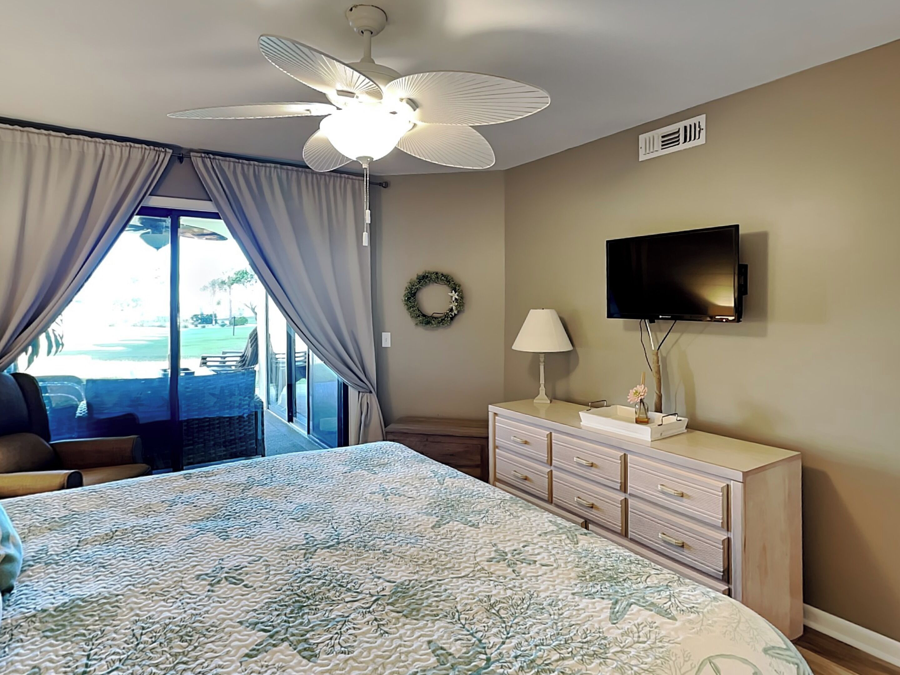 A hotel room with a bed, a TV, a dresser, and a view of a pool.