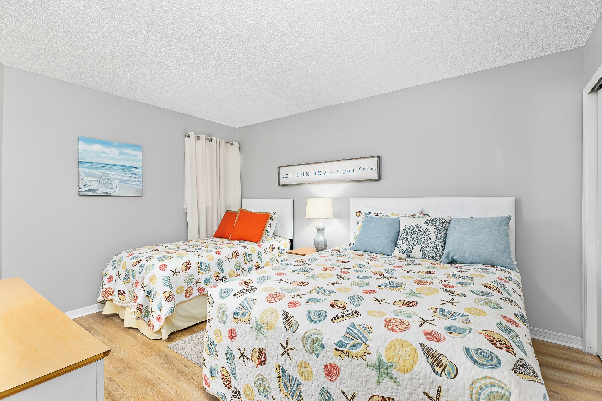 A bedroom with two beds, a nightstand, a lamp, and a framed quote on the wall.