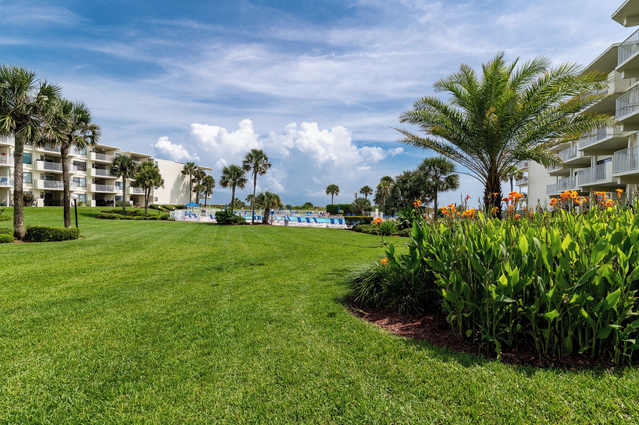 A well-maintained lawn, palm trees, and a pool area in a resort setting.