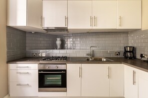 Uma cozinha com armários brancos, fogão de aço inoxidável, forno embutido, pia e cafeteira.