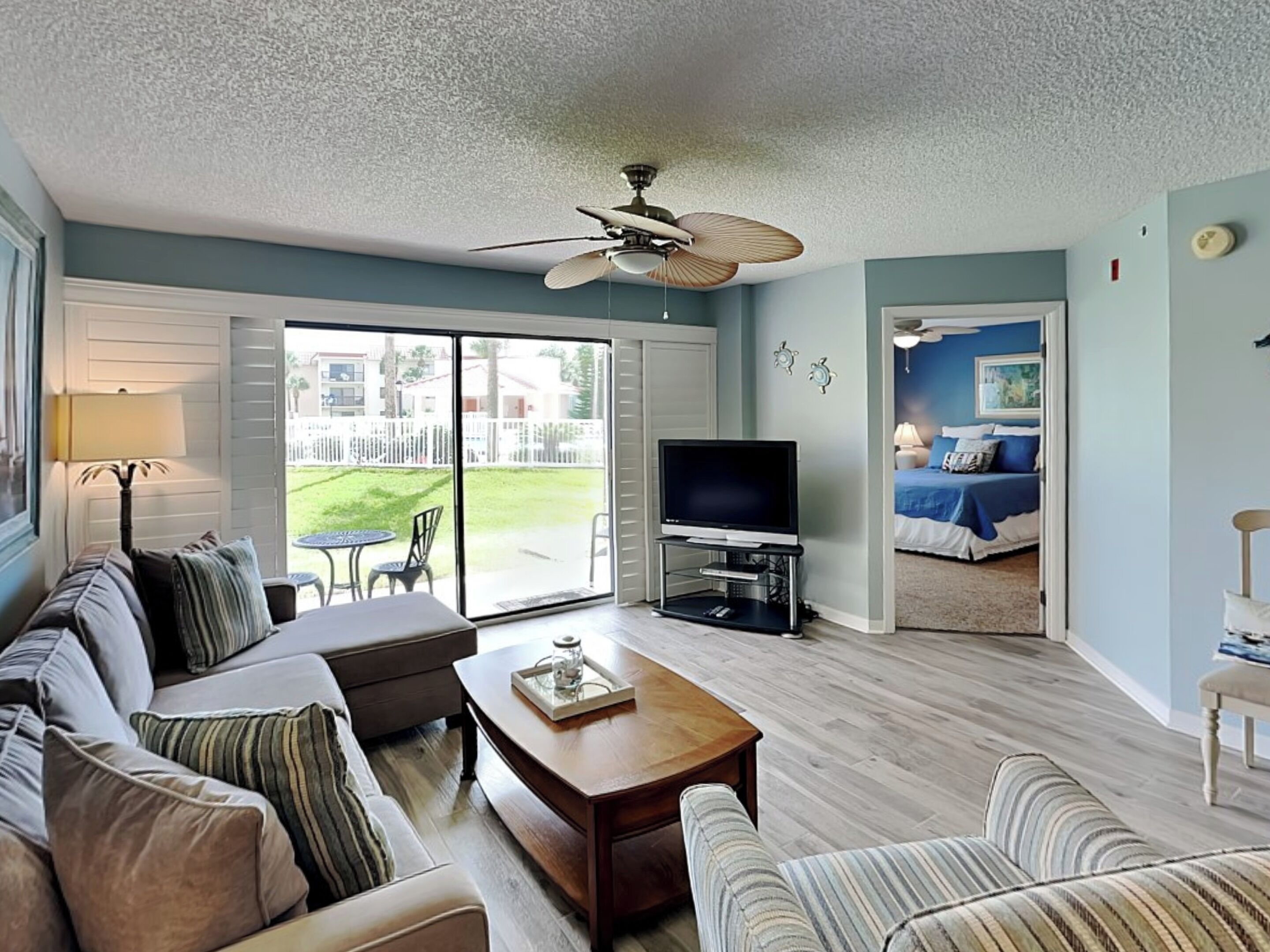 A living room with a sofa, coffee table, and TV. There is a sliding glass door leading to a balcony.