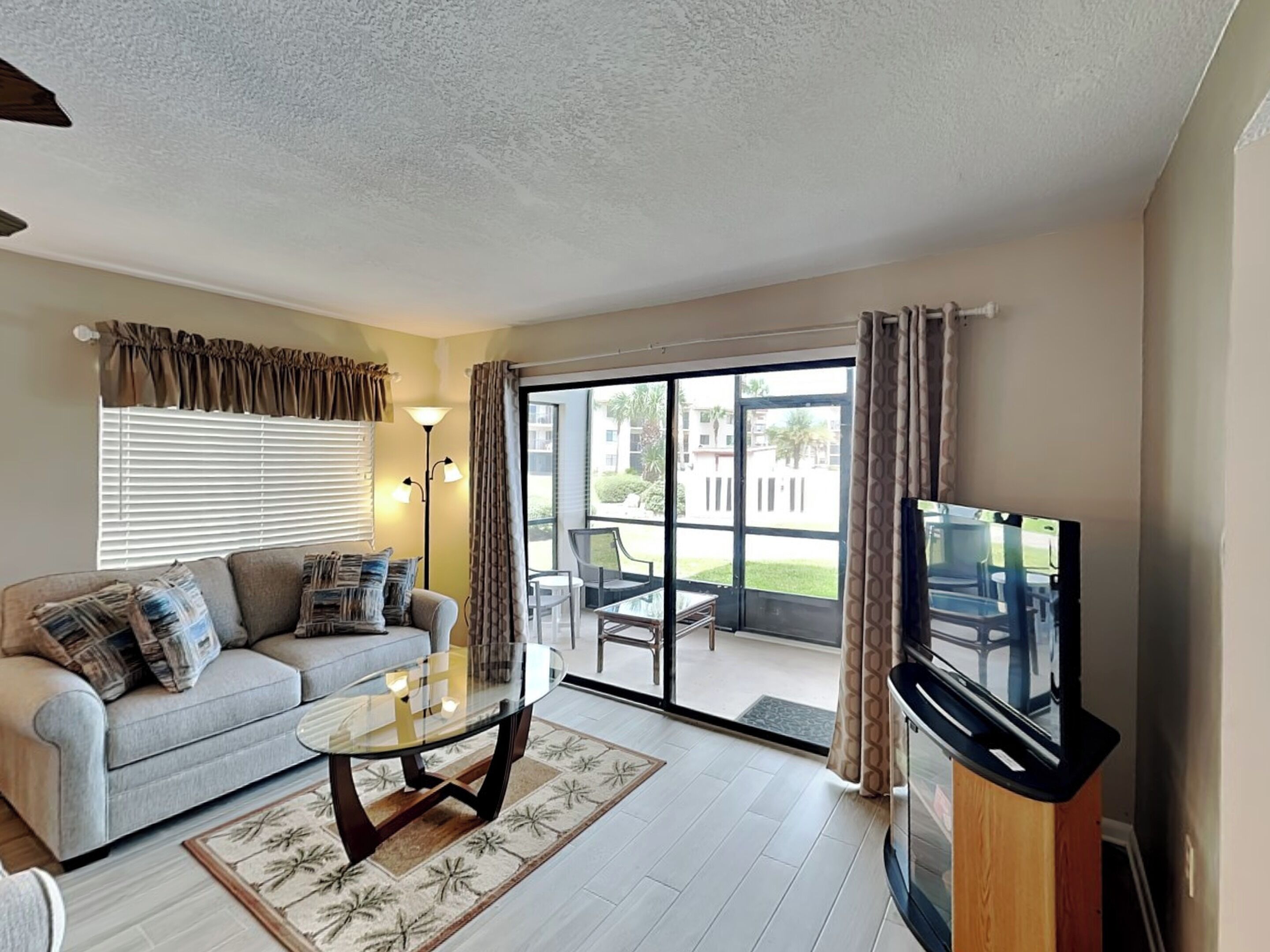 A living room with a sofa, a glass coffee table, a TV, and a balcony with outdoor furniture.