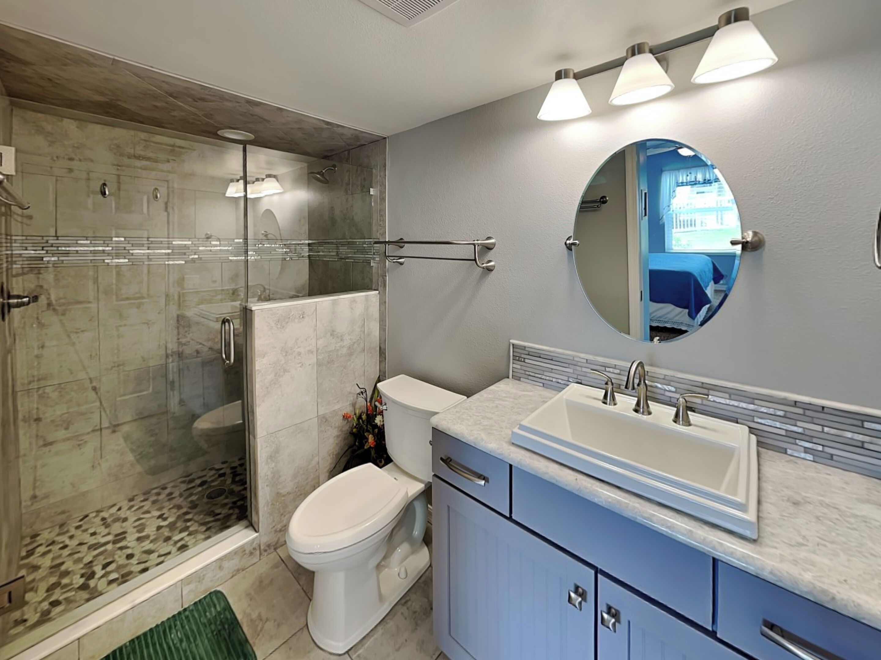 A modern bathroom with a glass-enclosed shower, a toilet, a sink with a mirror, and light-colored tiles.