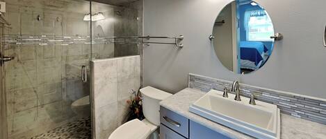 A modern bathroom with a glass-enclosed shower, a toilet, a sink with a mirror, and light-colored tiles.