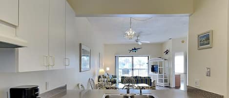 A kitchen with white cabinets, a coffee maker, a dishwasher, and a dining area with chairs and a table.