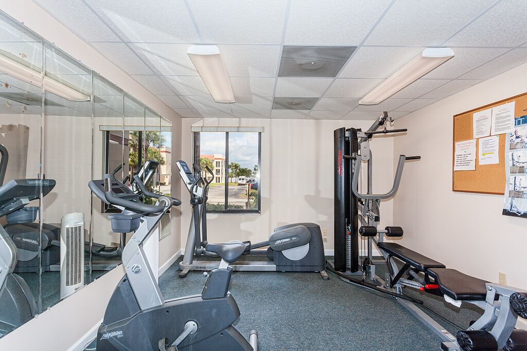 A gym with treadmills, elliptical machines, a bench press, and a wall-mounted mirror.