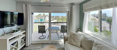 A living room with a TV, sofa, and a balcony with chairs.